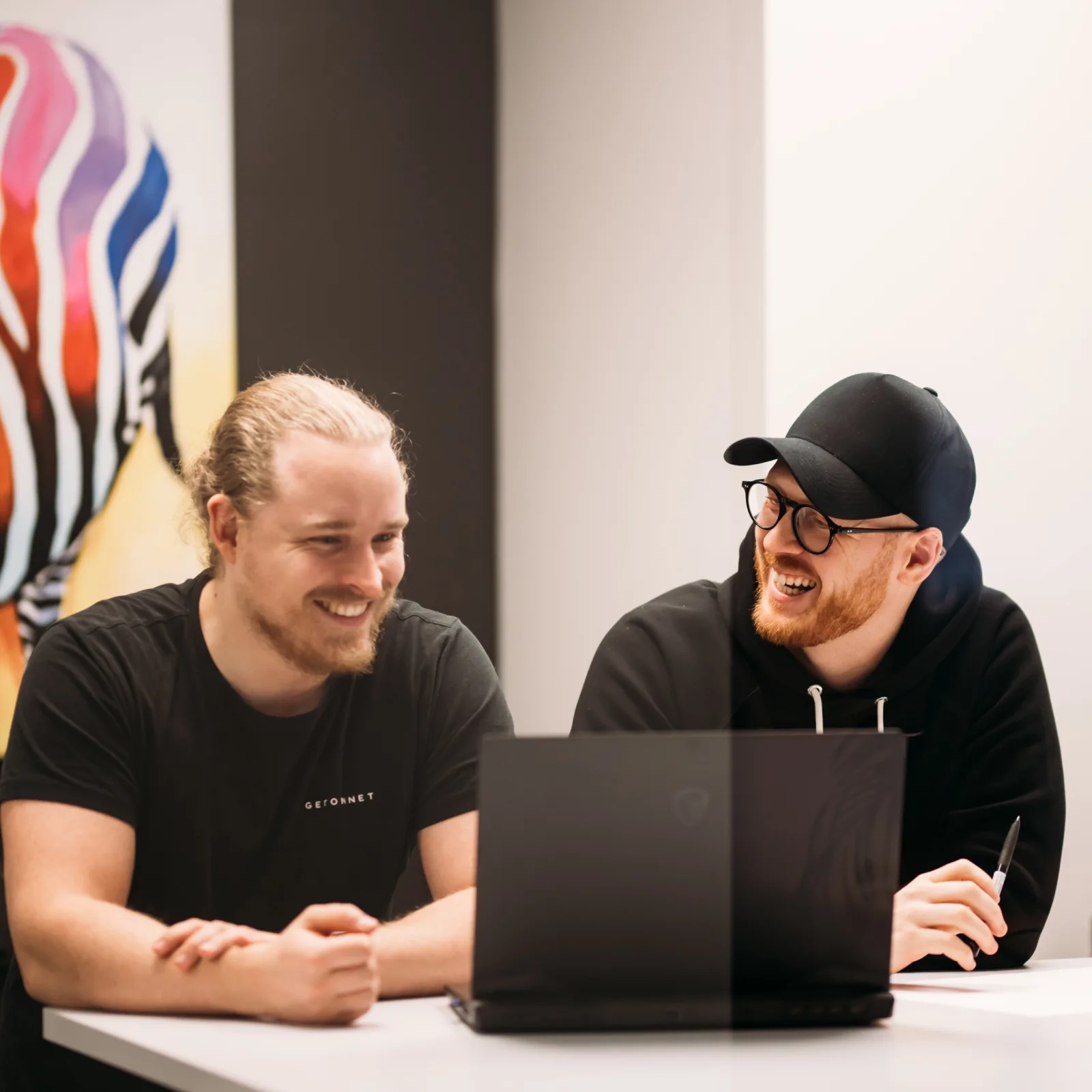 Två i teamet skrattar framför laptopen
