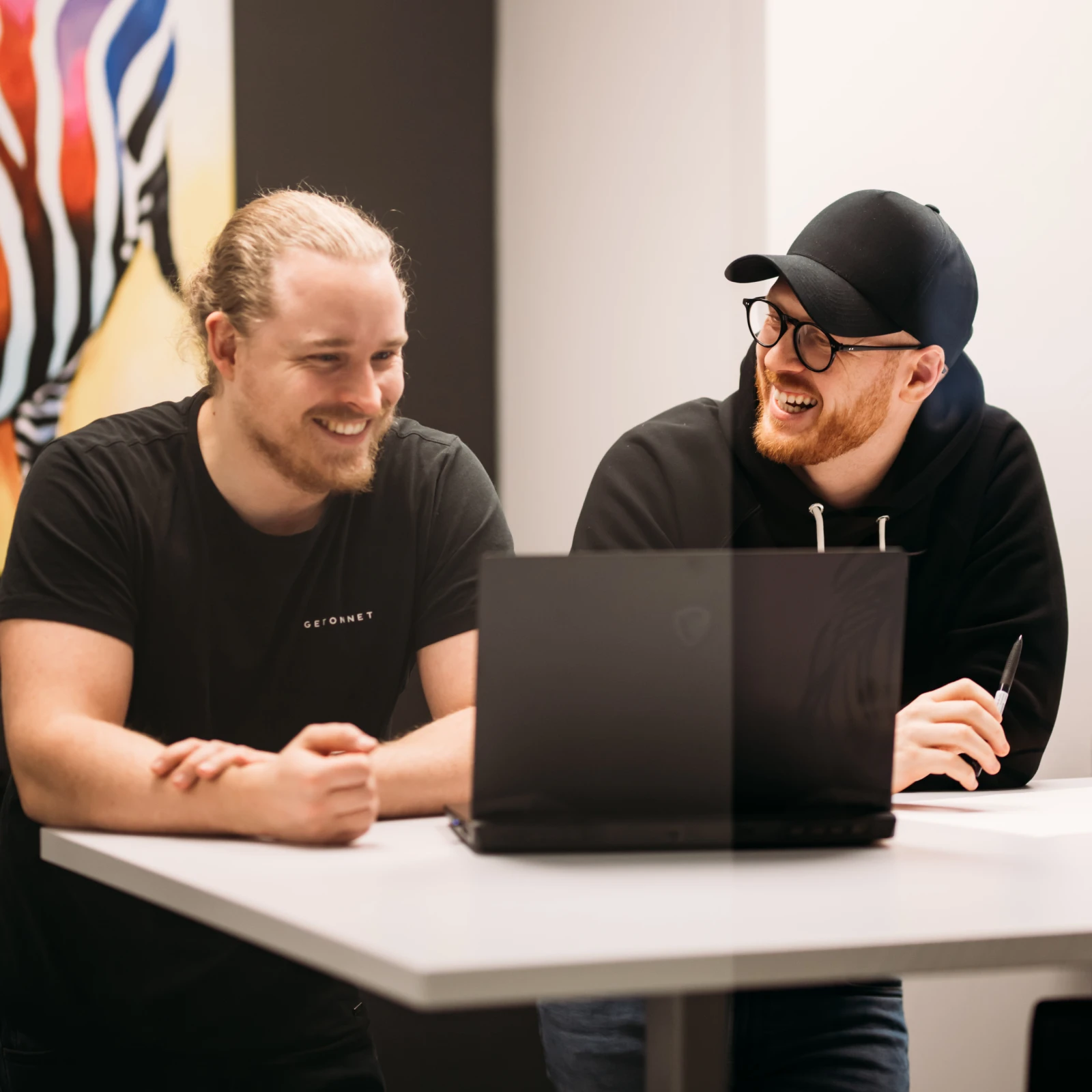 Två i teamet skrattar vid laptopen på kontoret